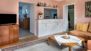 Un salon comprenant un téléviseur, un canapé, une table basse, et un coin cuisine visible à travers une porte ouverte.