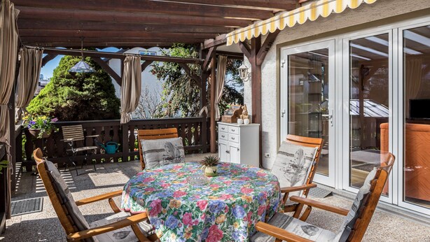 Une terrasse couverte avec une table ronde, des chaises en bois et un buffet blanc.