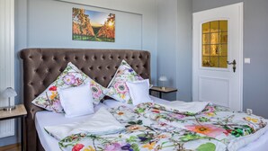 Une chambre à coucher avec une tête de lit capitonnée, une literie à motifs floraux, une table de chevet avec une lampe et une porte dotée d’un panneau en verre.