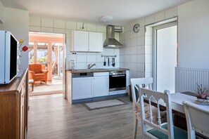 Moderni keittiö, jossa on valkoiset kaapit, sisäänrakennettu uuni sekä ruokailutila, jossa on pöytä ja tuolit.