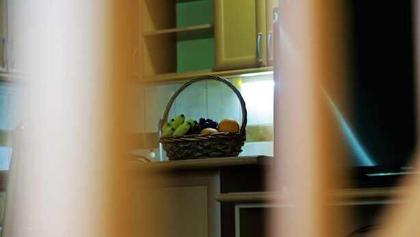 A kitchen with a wicker basket containing bananas, grapes, and an orange on the counter.