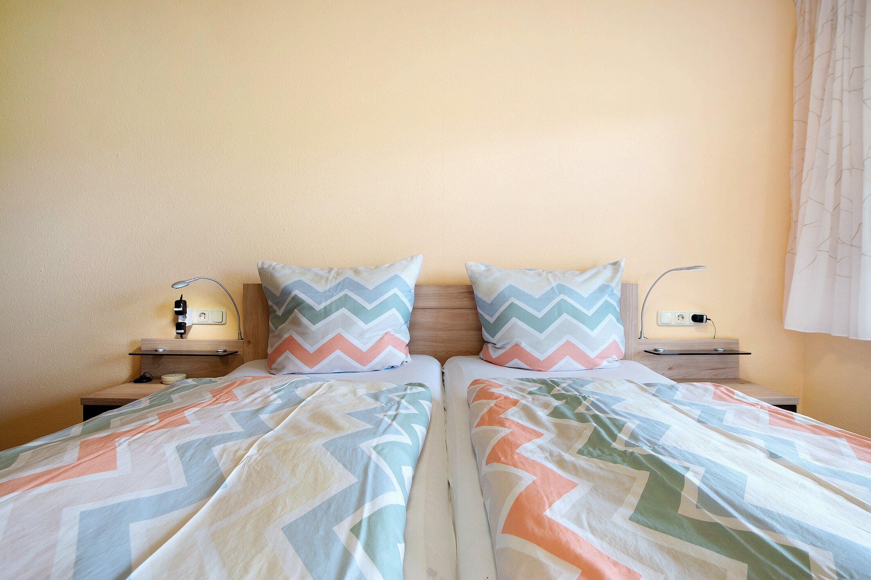 A double bed with patterned bedding, bedside tables with lamps, and a wall socket.