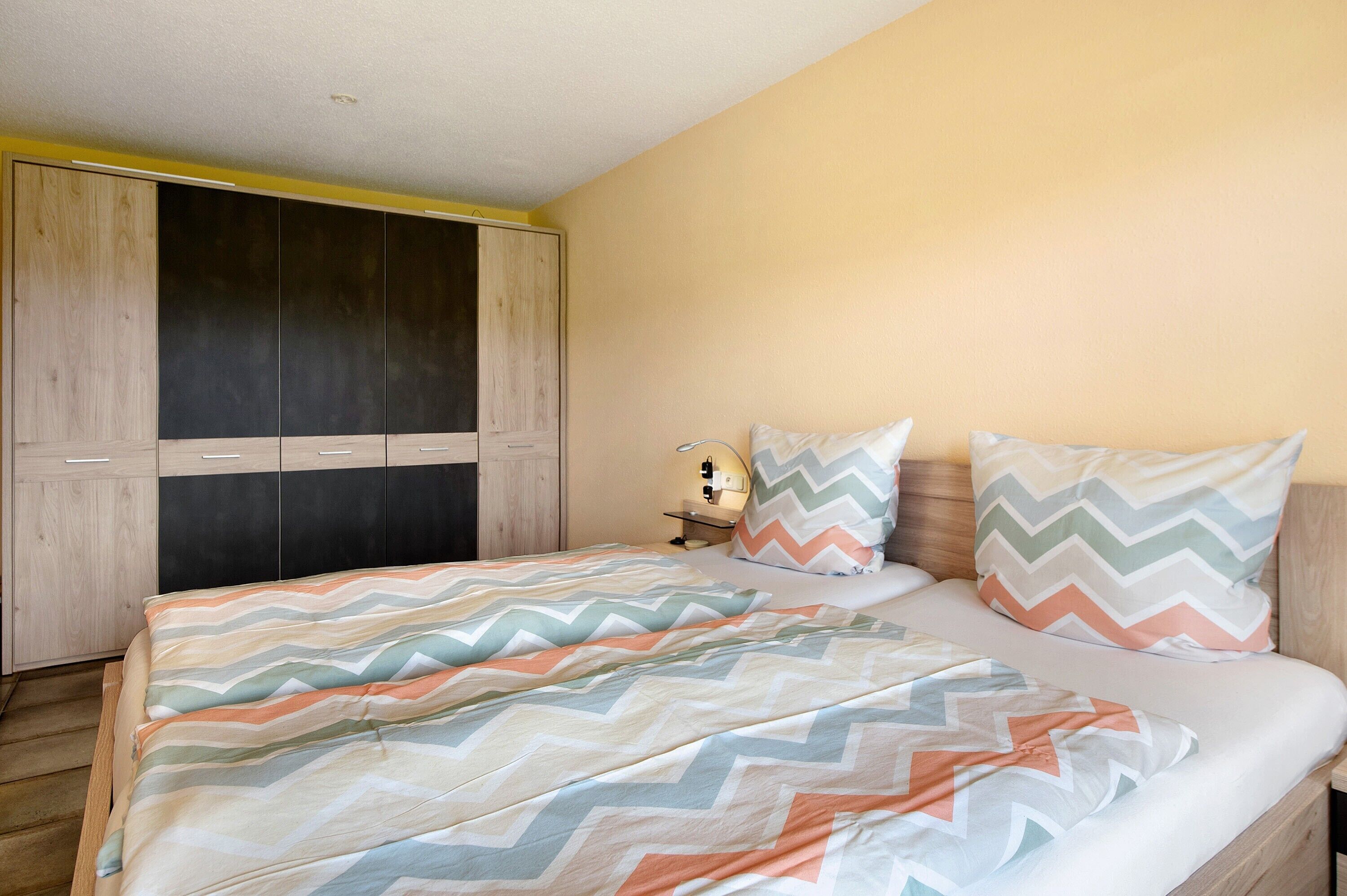 A bedroom with a bed, two pillows, a nightstand, and a wardrobe.