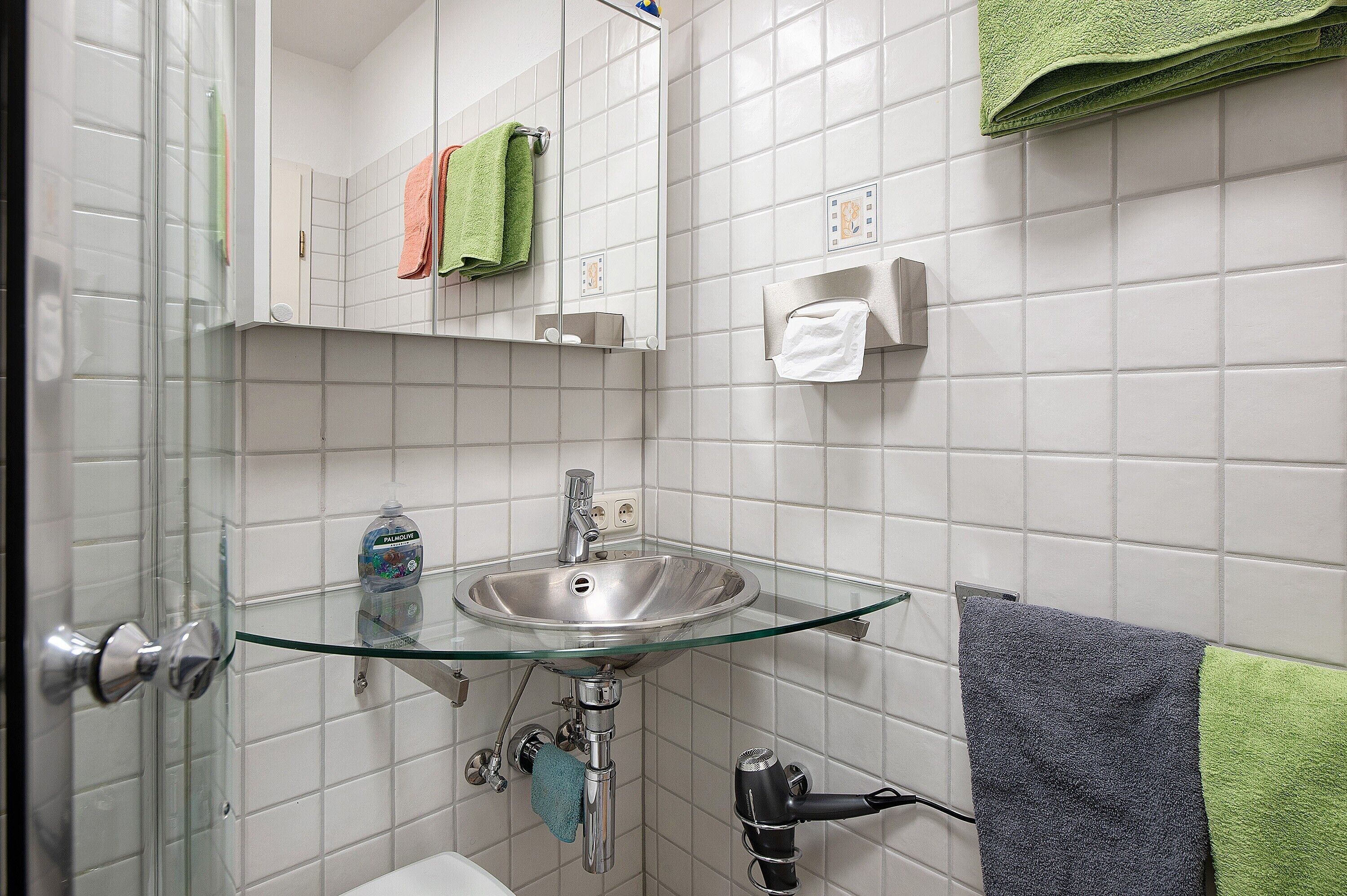 A bathroom with a glass sink, a mirror, a towel rack, and a towel hanging on the wall.