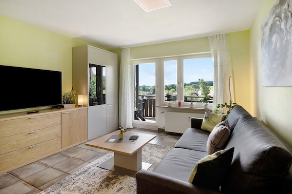 A living room with a TV, sofa, coffee table, and a view of the outdoors.