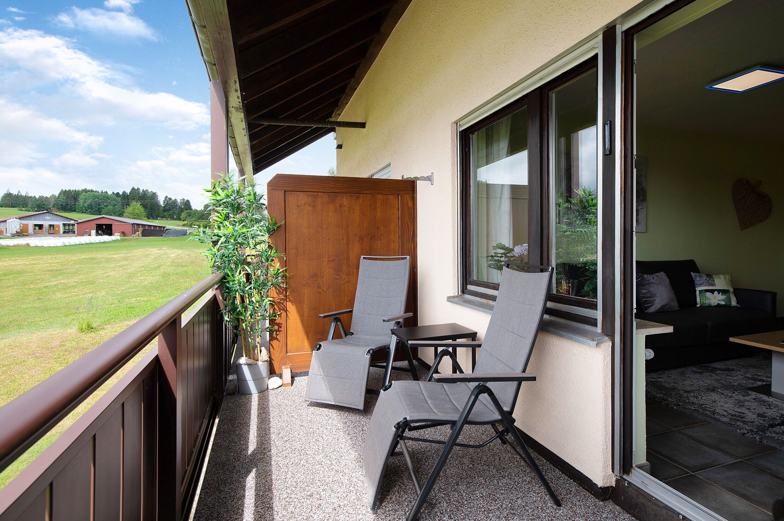 A balcony with two chairs, a small table, and a sliding glass door leading to a living area with a couch and a coffee table.