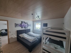 Ein Schlafzimmer mit Etagenbett, einer Schlafcouch, einem Nachttisch, einem Wandbild und einem Fenster.