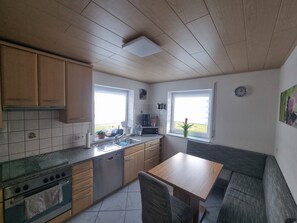 Eine Küche mit Holzausstattung, einem Geschirrspüler, einem Herd, einer Spüle, einem Fenster und einem Esstisch mit Stuhl.