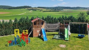 A playground with a slide, climbing structures, and a wooden playhouse. - Holiday Apartment "Biosphärenblick" with Private Terrace, Shared Garden and Wi-Fi (Münsingen)
