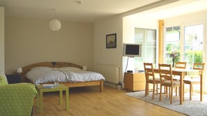 A bedroom with a bed, a desk with a chair, a TV, and a window with a view of greenery. - Studio 'Sandra Scheck' with Mountain View, Private Terrace & Wi-Fi (Lindau am Bodensee)