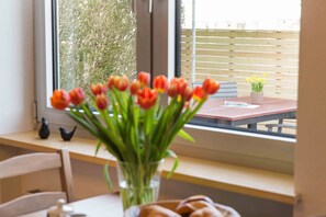 A window with a view of a wooden fence and greenery, a table with a vase of tulips, and a small potted plant.