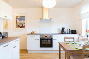 A modern kitchen with white cabinetry, a built-in oven, a coffee maker, and a dining area with a table set for two.