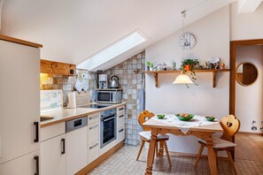 Une cuisine compacte équipée d’un lave-vaisselle, d’un four, d’un four à micro-ondes et d’une bouilloire. On y trouve une table à manger avec des chaises et un luminaire suspendu.