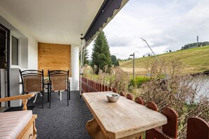 Une table en bois, des chaises et un bol, une fenêtre, et une vue sur un espace verdoyant avec un arbre.