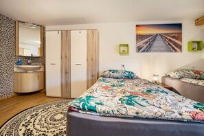 Une chambre à coucher comprenant un lit, une armoire, un miroir, un lavabo et un tableau représentant un coucher de soleil.