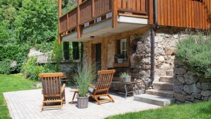 Un balcon en bois avec un mur en pierre, une chaise en bois et une plante en pot.