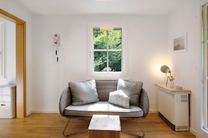 Un salon moderne avec un canapé, une petite table, un radiateur et une fenêtre donnant sur un espace verdoyant.
