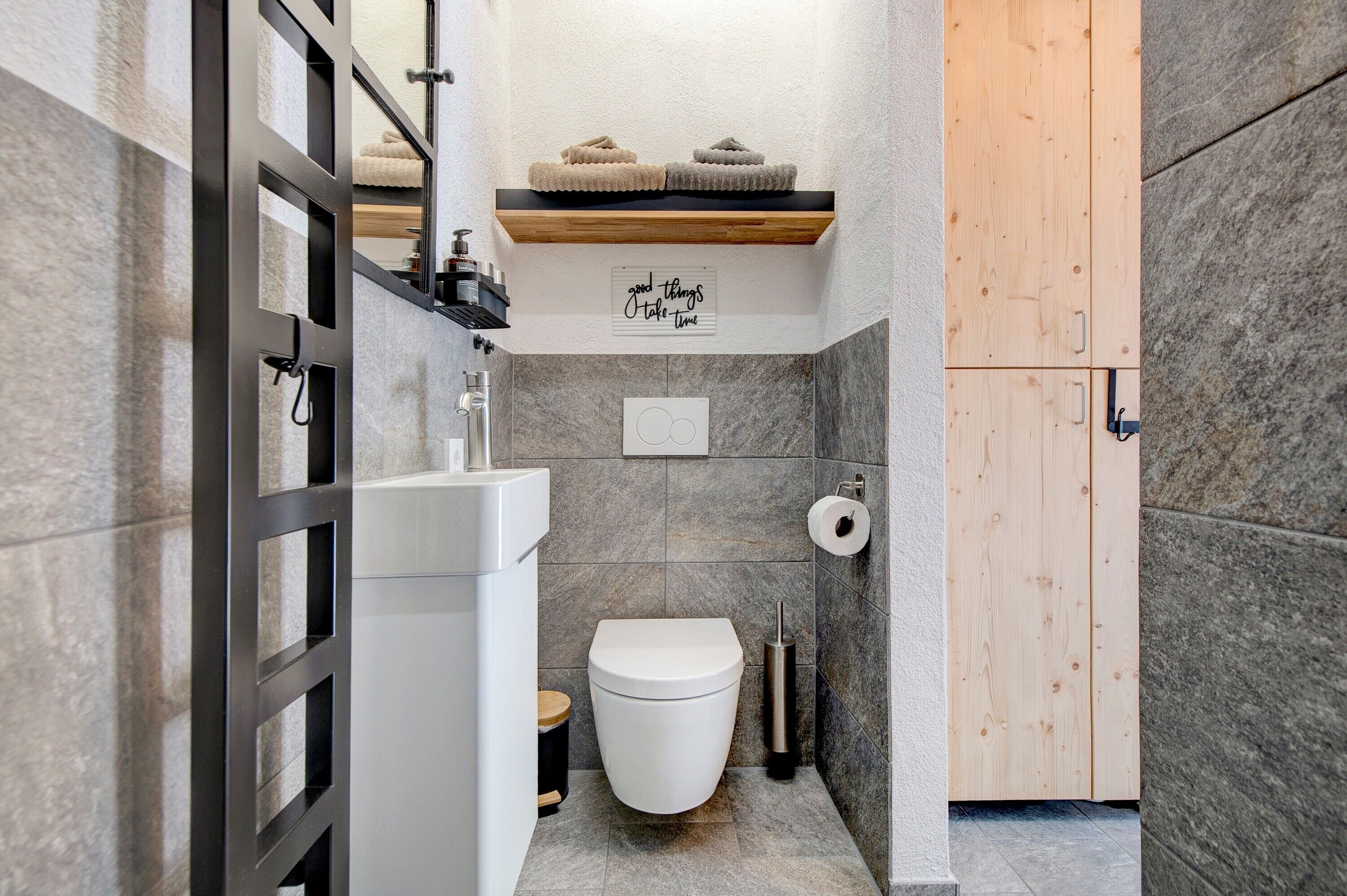 A bathroom with a toilet, sink, and shelf with towels.