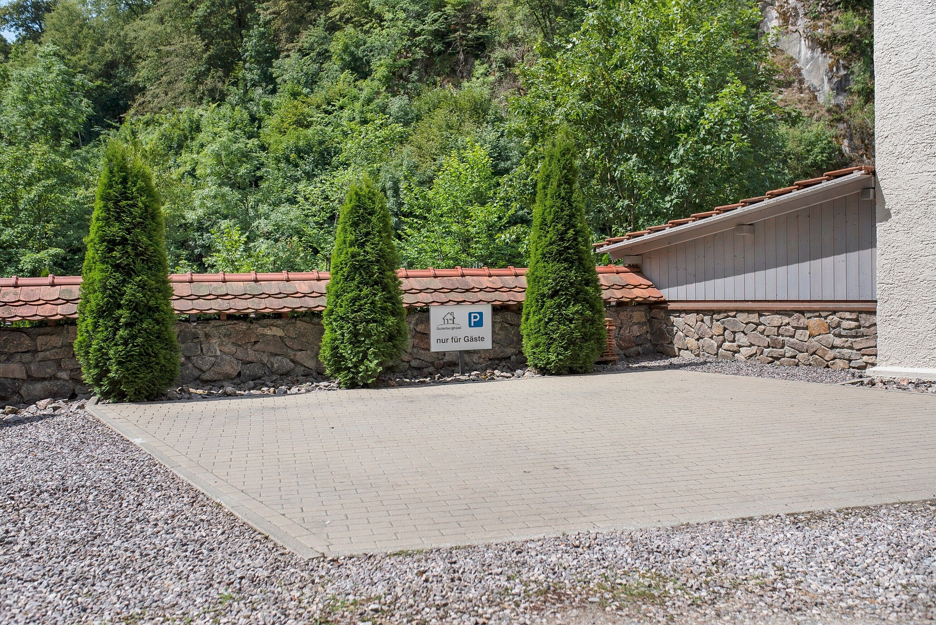 A paved parking area with a stone wall and a building with a red-tiled roof.