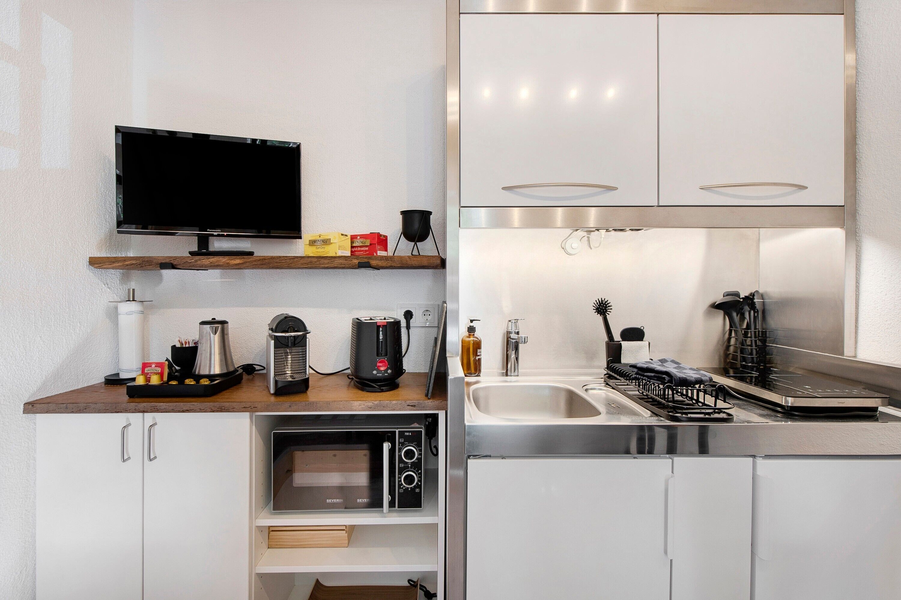 A modern kitchen with a flat-screen TV, a coffee maker, a toaster, a kettle, a microwave, and a dishwasher.