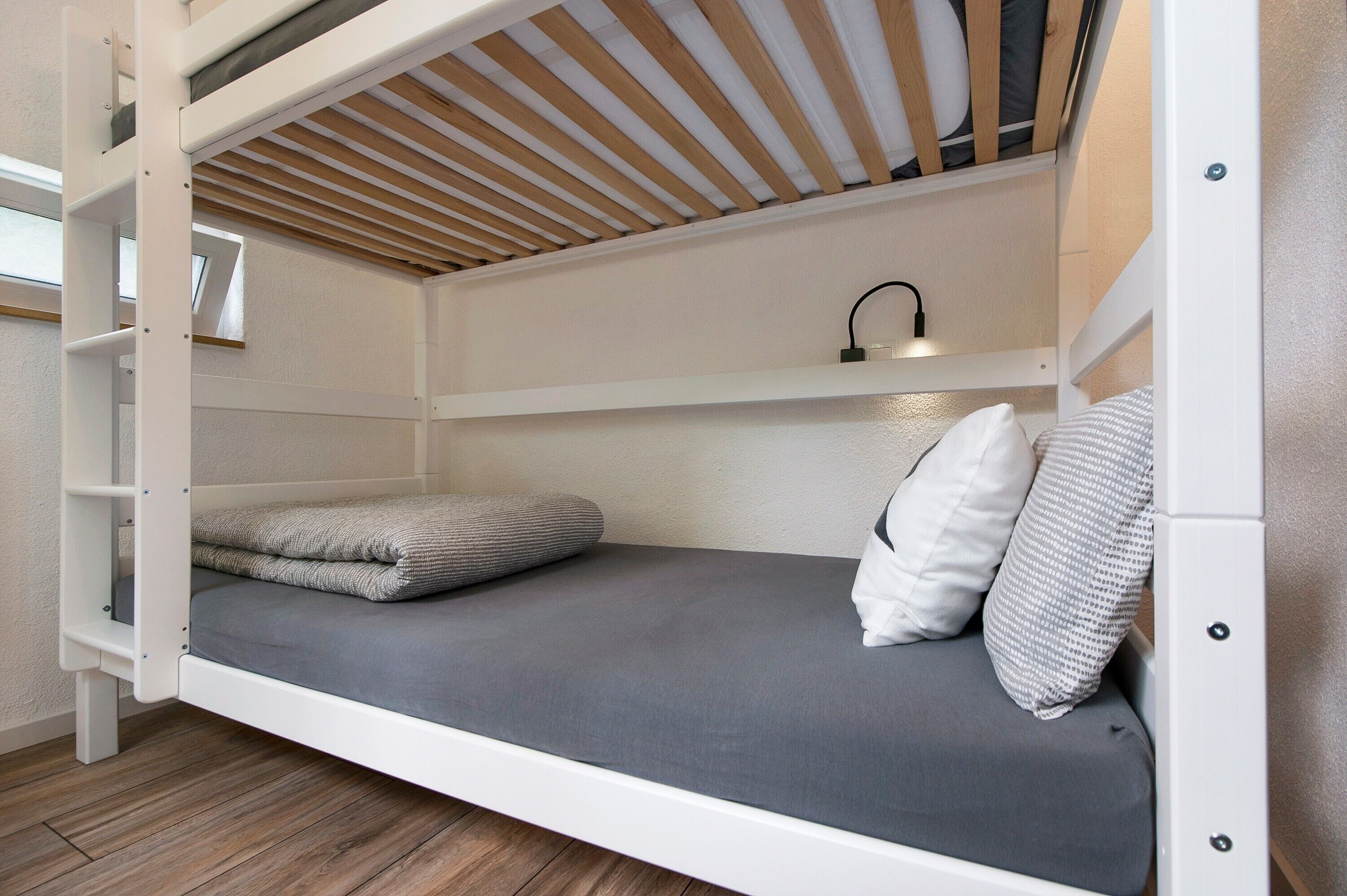 Een stapelbed met een uittrekbaar bureau, een plank erboven en een kleine lamp.