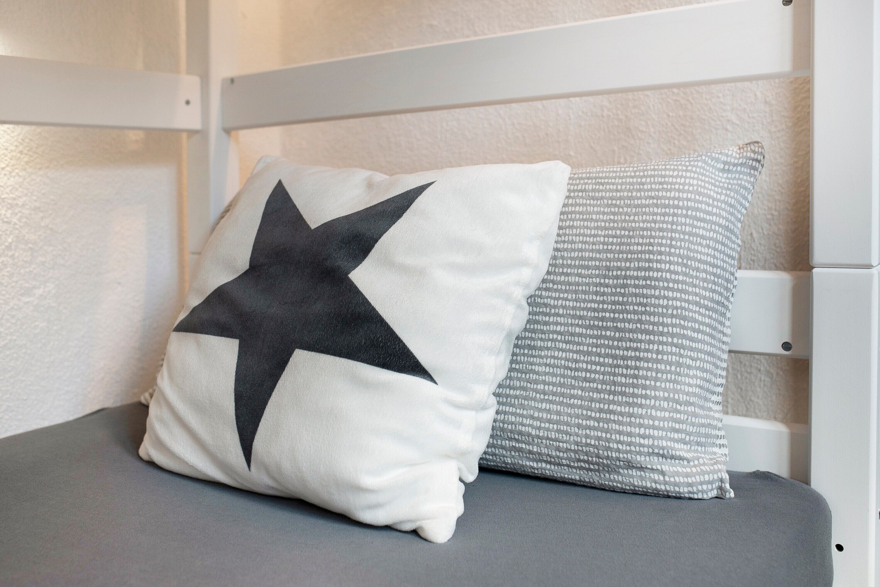 Un lit avec un matelas gris et deux oreillers, l’un orné d’une étoile noire et l’autre d’un motif blanc.