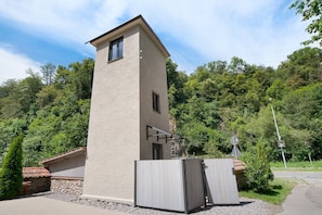 A modern building with a tower-like structure, a gated entrance, and a stone wall.