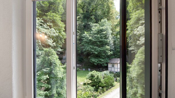 Vista attraverso un'ampia vetrata scorrevole su un giardino e una piccola casa.