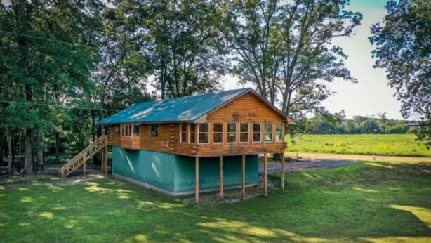 A wooden cabin with a green roof, a wooden deck, and a staircase leading to the entrance.