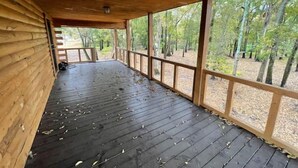 A covered wooden deck with a view of a forest.