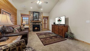 A living room with a fireplace, a ceiling fan, a television, and a couch.