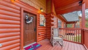 A log cabin with a wooden porch, a rocking chair, and a welcome sign.