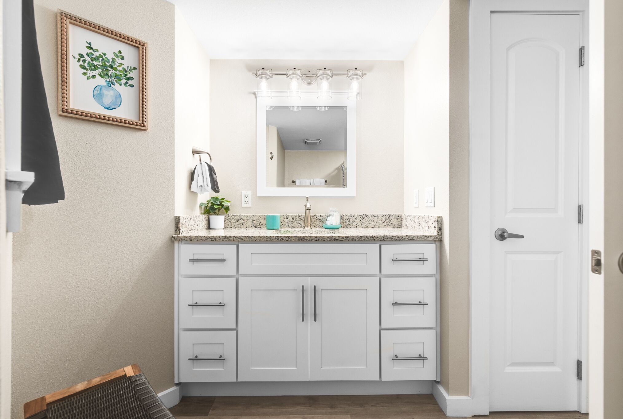A bathroom with a white vanity, a mirror, and a door.