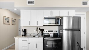A modern kitchen with white cabinets, a stainless steel refrigerator, a microwave, and a stove. - Sandcastle Condominiums Unit 217 (Port Aransas)