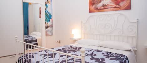 A bedroom with a bed, a nightstand, a mirror, and a painting on the wall.