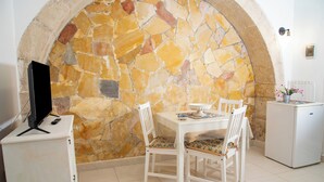 Comedor con pared de piedra, mobiliario blanco y un refrigerador pequeño.