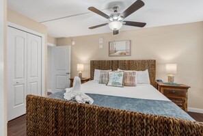 A hotel room with a bed, a ceiling fan, a nightstand with a lamp, and a door.