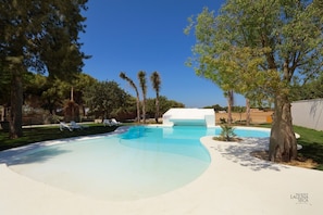 A swimming pool with lounge chairs, surrounded by trees and a white building.