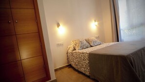 A bedroom with a bed, patterned bedding, a wardrobe, and wall-mounted lights. - Hibiscus Apartment with Shared Pool (Chiclana de la Frontera)