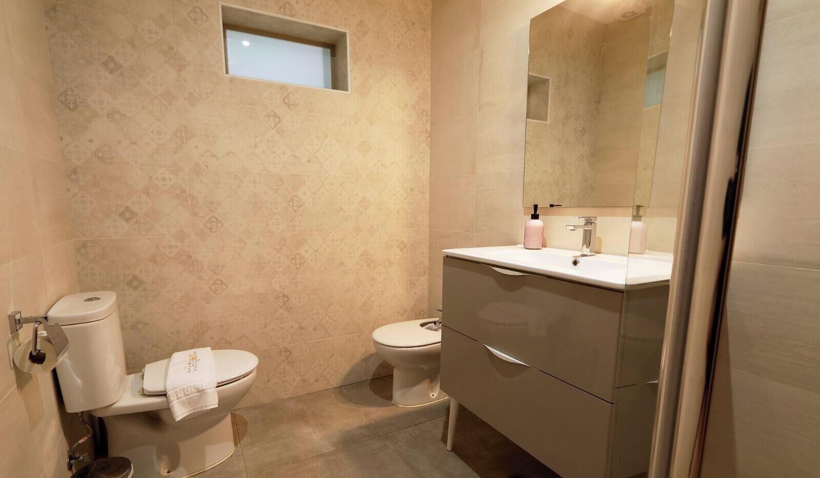 A bathroom with a toilet, bidet, and vanity with a mirror.