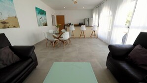 A modern living room with a dining area, a kitchen in the background, and large windows. - Buganvilla Apartment with Shared Pool (Chiclana de la Frontera)