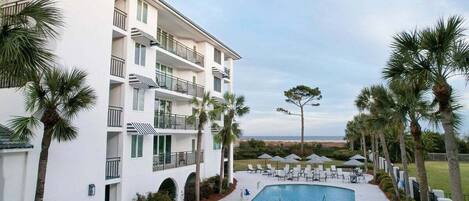 A hotel with a pool area, outdoor seating, and palm trees.
