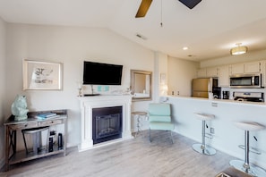 A modern kitchen with a flat-screen TV, a fireplace, bar stools, and a dining area.