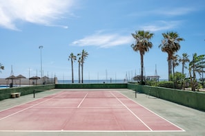 Un campo da tennis con una rete, circondato da palme e vista sul mare.