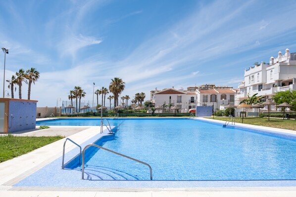 A swimming pool with a clear blue sky, surrounded by palm trees and white buildings. - Apartment 'Las Terrazas Primera Línea de Playa' with Sea View, Wi-Fi and Air Conditioning (Mezquitilla)