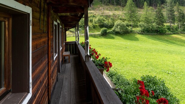A wooden cabin with a balcony overlooking a green landscape.