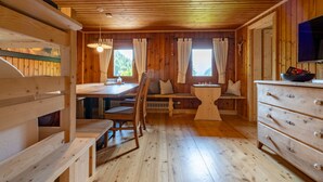 A wooden cabin interior with a dining table, benches, a dresser, and a television.