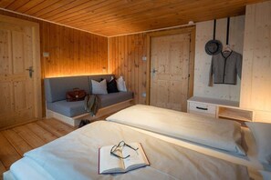 A cozy room with wooden walls, a sofa, two beds, a small table, and a hanging hat. - Chalet 'Kasern' with Mountain View, Private Terrace and Wi-Fi (Gais)