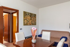 Un coin repas avec une table en bois, des chaises, un vase de fleurs, un tableau au mur et un canapé.