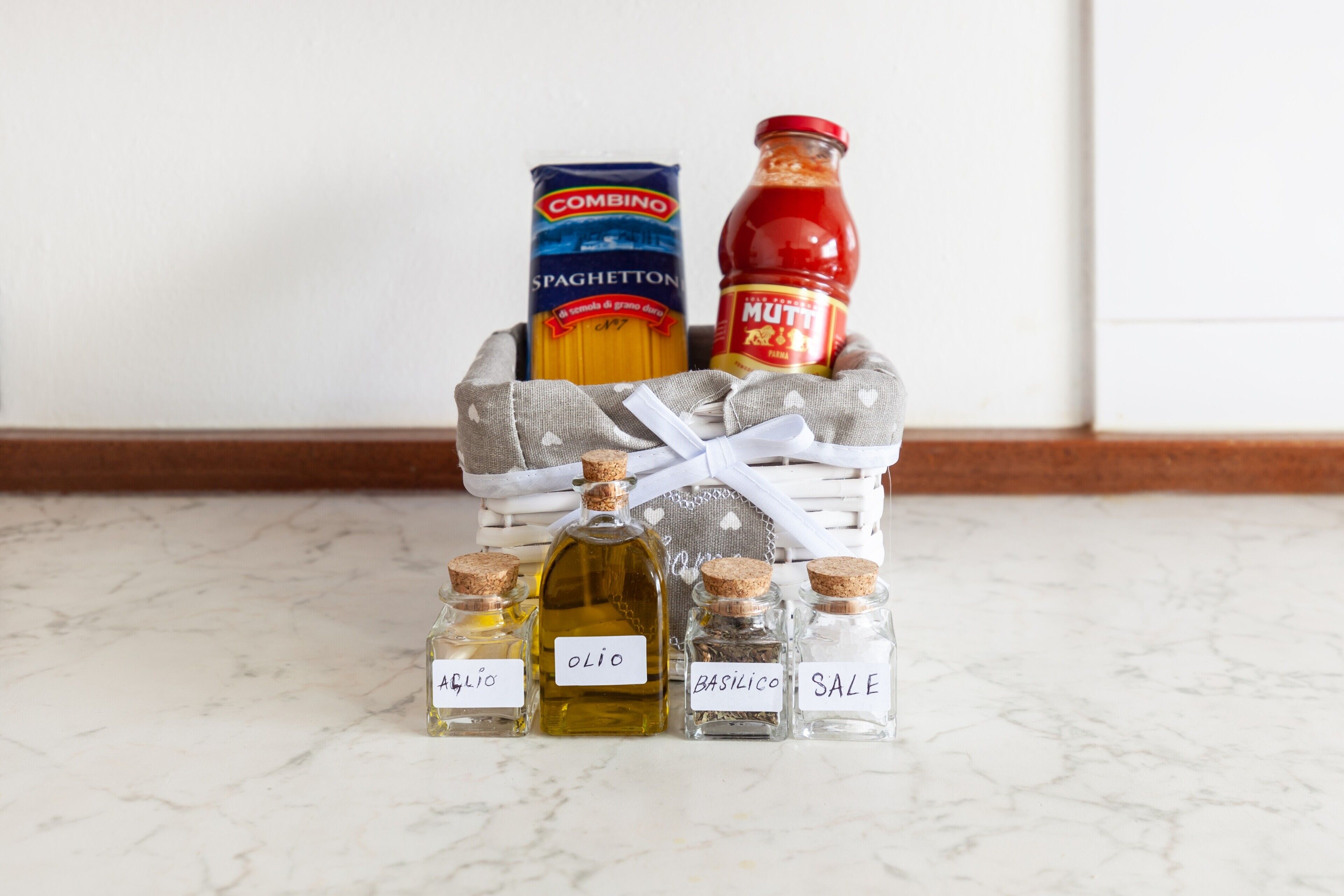 Una encimera de cocina con una caja de pasta, una botella de salsa y cuatro botellas etiquetadas de aceite, aceite de oliva, albahaca y sal.